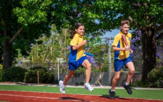 Students run a relay on a school athletics track.
